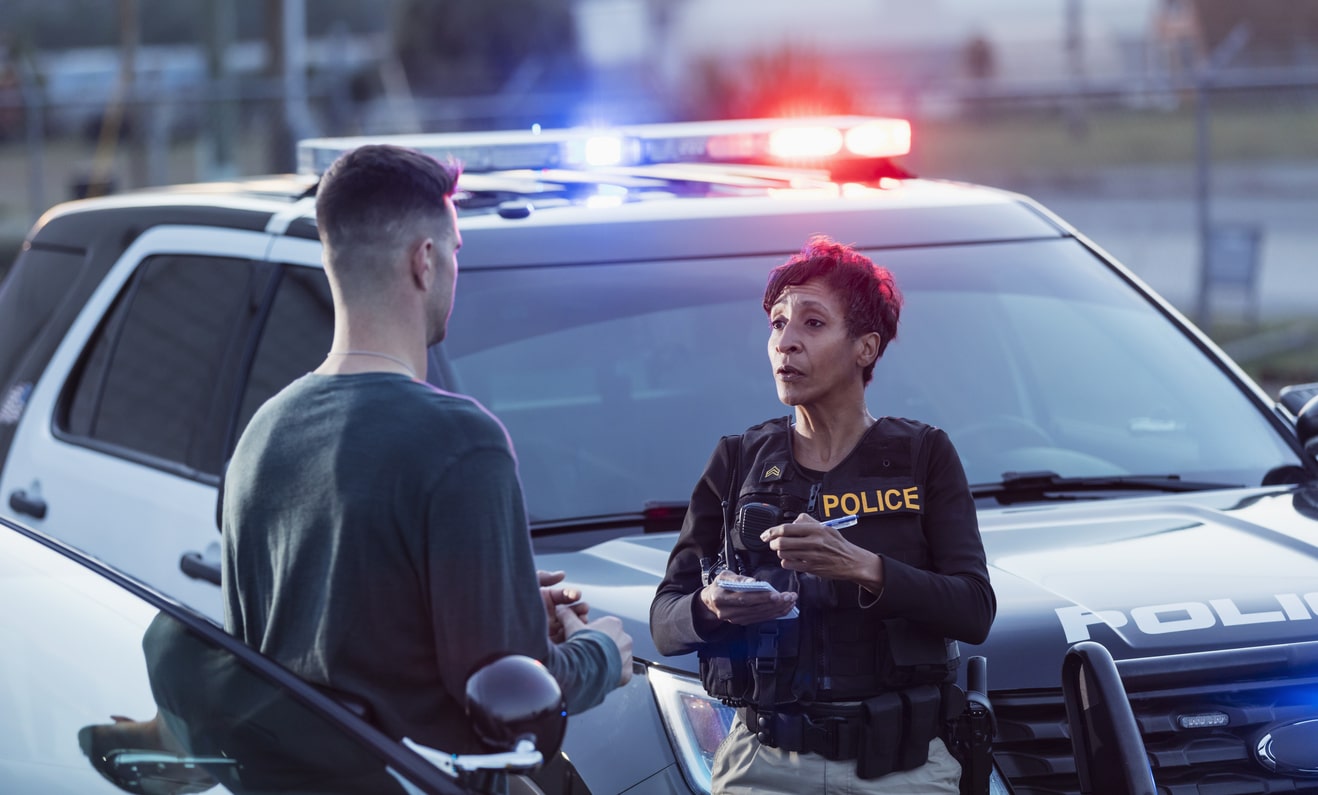 Policewoman taking a statement from a young driver beside a patrol car